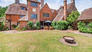 A large brick house with a well-maintained lawn, outdoor seating area, and a fire pit. - Large Tudor Manor House with Private Jacuzzi & Indoor Pool, Sleeps Max 20. (Hailsham)