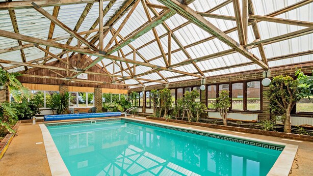 An indoor swimming pool with a wooden roof structure and surrounding greenery. - Large Tudor Manor House with Private Jacuzzi & Indoor Pool, Sleeps Max 20. (Hailsham)