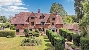 A large, brick house with multiple chimneys, surrounded by well-maintained gardens and hedges. - Large Tudor Manor House with Private Jacuzzi & Indoor Pool, Sleeps Max 20. (Hailsham)