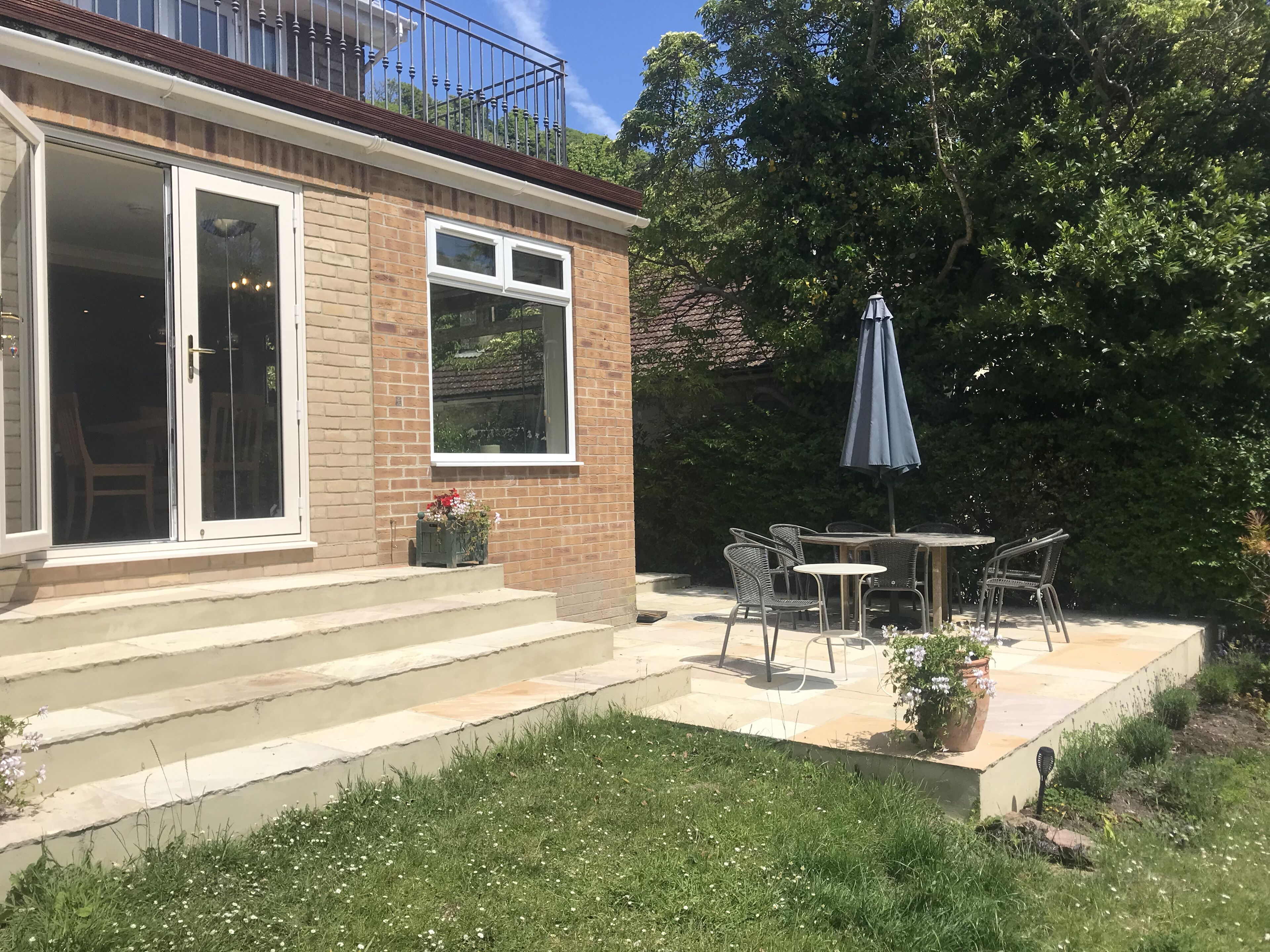 Un patio con tavolo e sedie, una pianta in vaso e una finestra che si affaccia su un giardino.