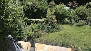 Un patio exterior con una mesa redonda y cuatro sillas, rodeado por un jardín con diversas plantas y flores.