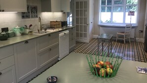 Una cocina moderna con armarios blancos, salpicadero azulejado, zona de comedor con mesa y sillas, y ventana con vistas a zonas verdes.