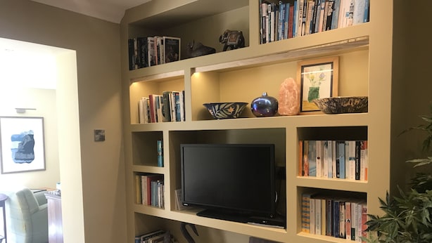 Una estantería con libros, objetos decorativos y un televisor.