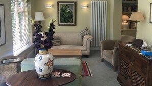 Una sala de estar con un sofá, sillones, una mesa de centro, un jarrón con flores, una estantería y un radiador.