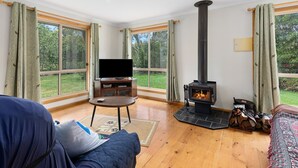 A cozy living room with a fireplace, a television, and a large window offering a view of the outdoors. - PET FRIENDLY COTTAGES - COLLIE COTTAGE- 4 STAR SELF CONTAINED COTTAGES (Worrolong)