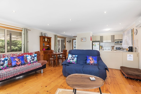 A cozy living room with a blue sofa, a wooden coffee table, and a dining area with a wooden cabinet and chairs.
