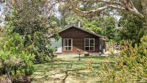 A small, single-story wooden house with a sloped roof, surrounded by dense greenery and trees. - PET FRIENDLY COTTAGES - COLLIE COTTAGE- 4 STAR SELF CONTAINED COTTAGES (Worrolong)