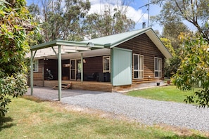A wooden cabin with a covered porch, a gravel driveway, and surrounding trees.