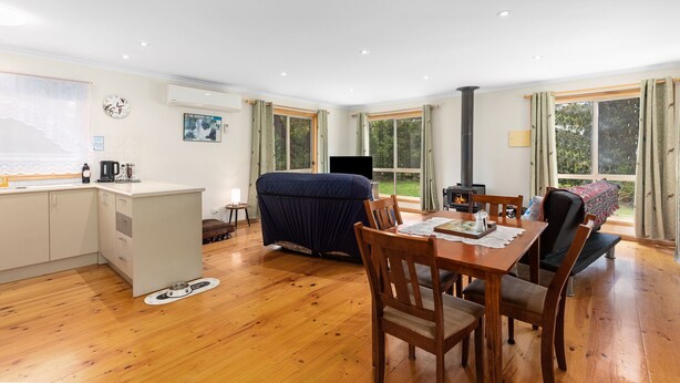 A cozy room with a wooden floor, a dining table with chairs, a sofa, a TV, a fireplace, and a kitchen area with a sink and cabinets. - PET FRIENDLY COTTAGES - COLLIE COTTAGE- 4 STAR SELF CONTAINED COTTAGES (Worrolong)