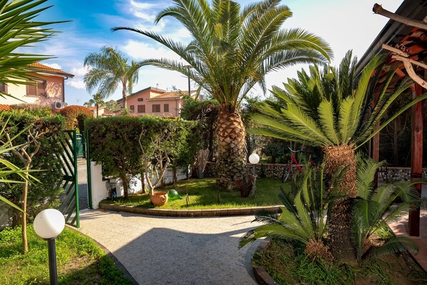 A garden with palm trees, a paved pathway, and a building in the background.