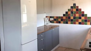 Una cocina con un refrigerador blanco, gabinetes grises, una encimera de madera y un salpicadero de mosaicos coloridos.