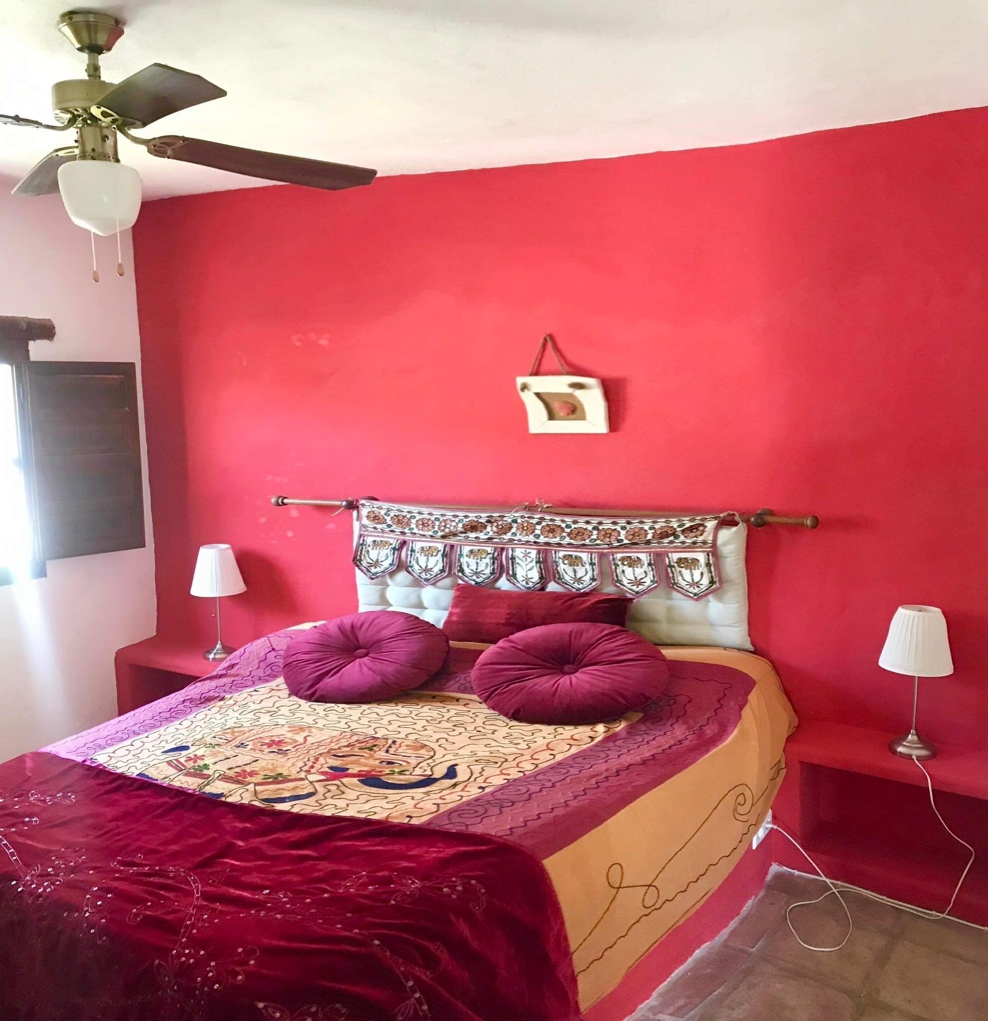 Una habitación con una cama, dos lámparas de noche, un ventilador de techo y una pared roja.