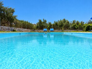 A clear blue pool with two blue lounge chairs and a stone wall in the background.