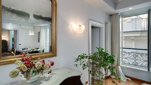 A room with a large mirror, a vase with flowers, a potted plant, and a view of the outside balcony. - TREVI FOUNTAIN 3 BEDROOM APARTMENT PRESTIGIOUS. (Roma)