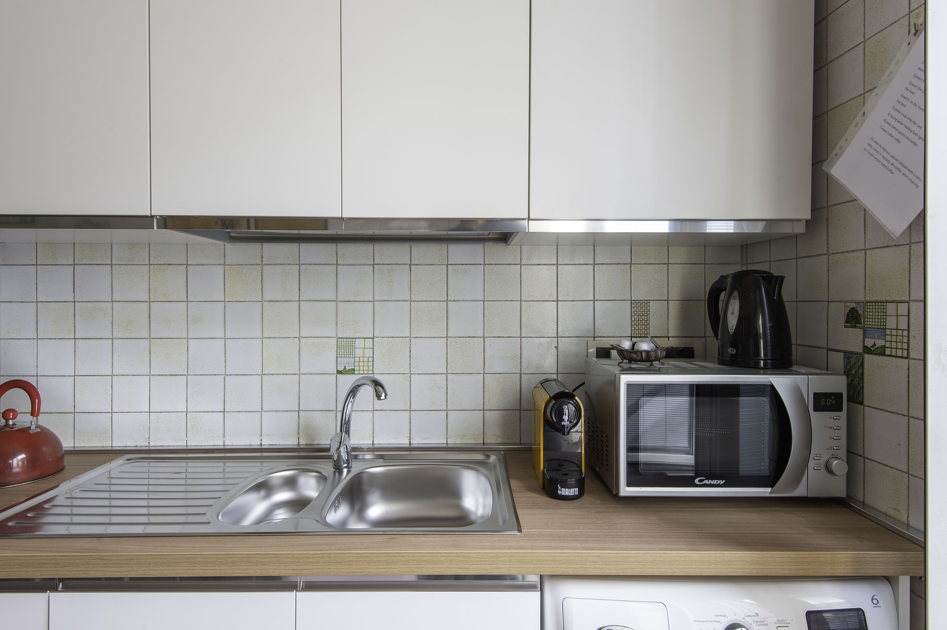 A kitchen with a stainless steel sink, a kettle, a toaster, and a microwave.