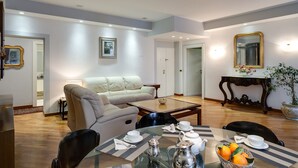 A modern living room with a sofa, dining table, and chairs. There is a coffee table with a teapot and cups. A potted plant is on a side table. - TREVI FOUNTAIN 3 BEDROOM APARTMENT PRESTIGIOUS. (Roma)