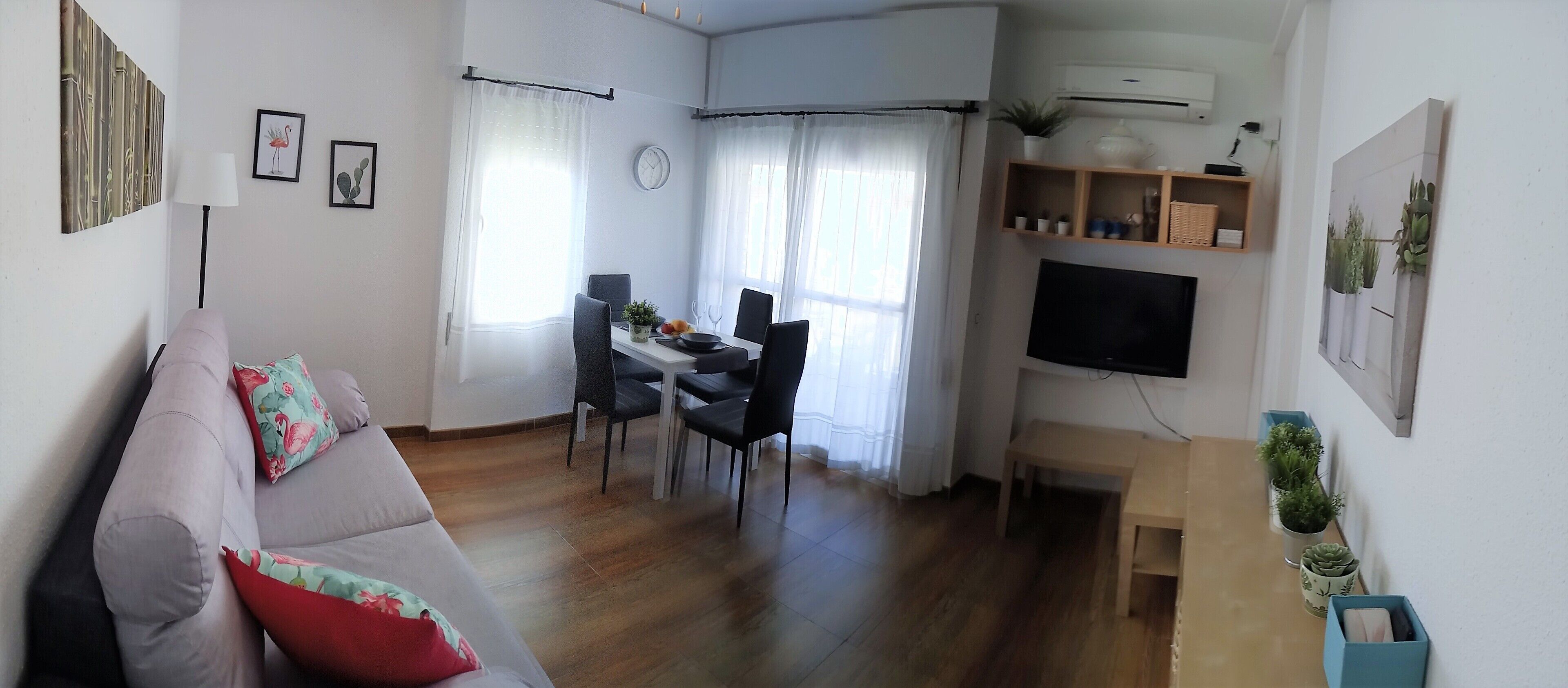 Ein Wohnzimmer mit einer Couch, einem Essbereich mit Stühlen, einem Fernseher und einem Fenster mit Vorhängen.