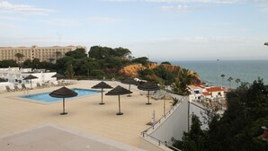 A pool area with umbrellas, lounge chairs, and a view of the sea and buildings. - Varandas do Mar T1_T, frente mar, Olhos de Água (Albufeira)