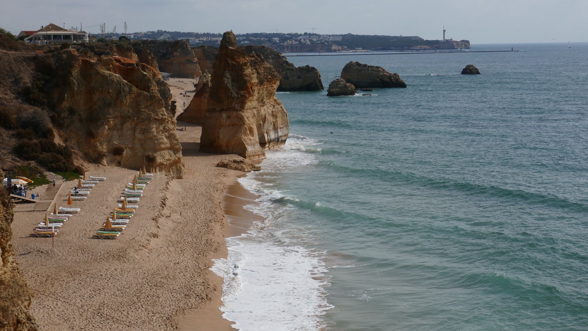 A beach with rocky cliffs, a row of beach umbrellas, and a view of the sea.