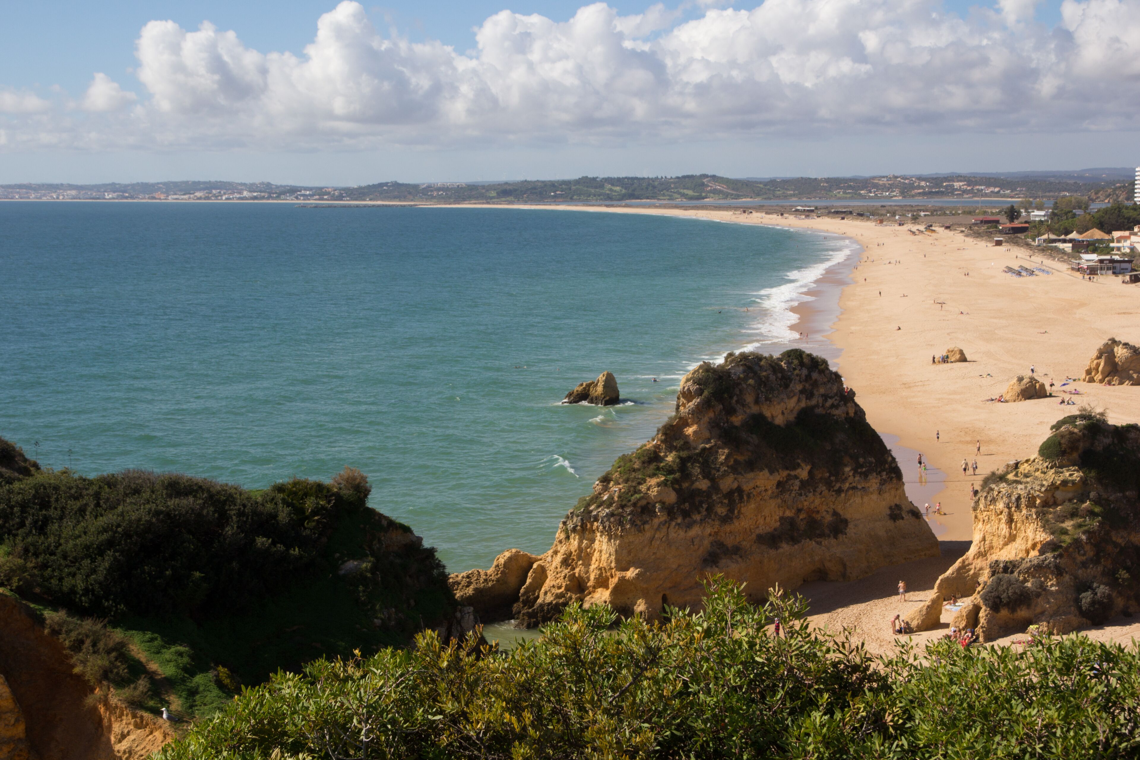 A coastal landscape with a sandy beach, rocky outcrops, and a clear view of the sea.