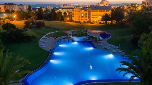 Une grande piscine à la forme incurvée, entourée de chaises longues et de palmiers.