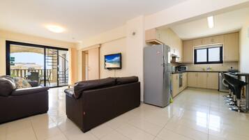 Una sala de estar moderna con sofá y televisor de pantalla plana, una cocina con refrigerador y microondas, y un balcón con vistas.