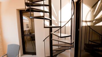 Una escalera en espiral en un interior moderno con mobiliario de mimbre y un ventanal que da a otra habitación.