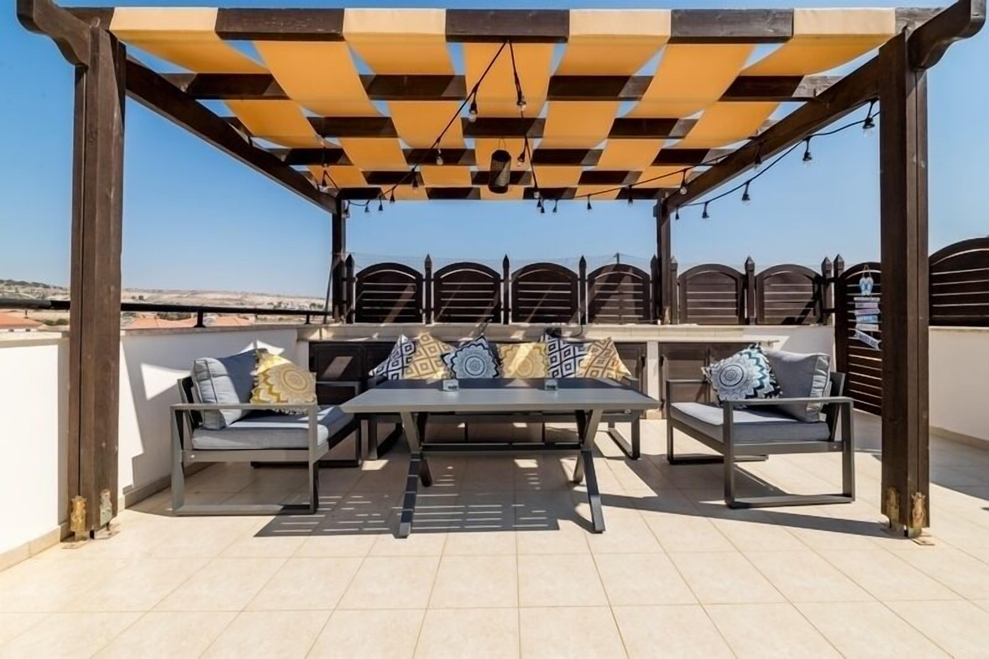 An outdoor seating area with a pergola, cushioned seating, and a view of the landscape.