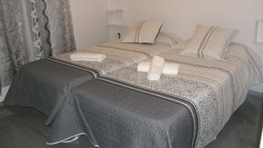 Een tweepersoonsbed met een bed met een patroon erop, twee kussens, een nachtkastje met een lamp en een raam met gordijnen.