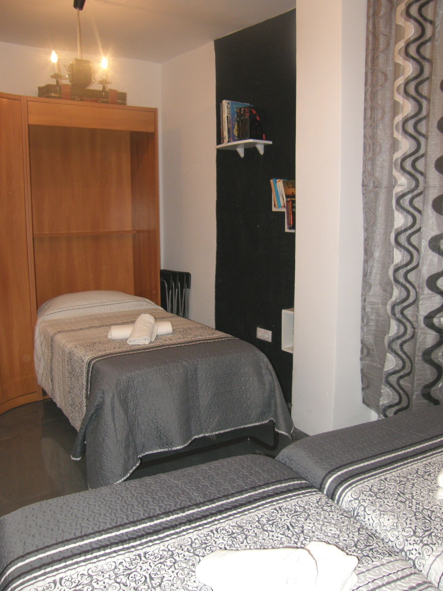 Une chambre avec deux lits, une armoire en bois, une étagère remplie de livres et un rideau à motifs.
