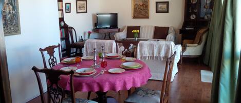 Un comedor con una mesa dispuesta para cuatro personas, rodeada de sillas de madera. Un televisor está montado en la pared sobre la mesa.