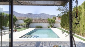 Piscina con sillones reclinables, una pérgola y vistas a las montañas.