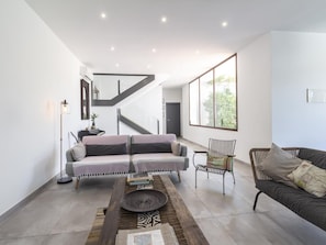 A modern living room with a sofa, a chair, a coffee table, and a staircase.