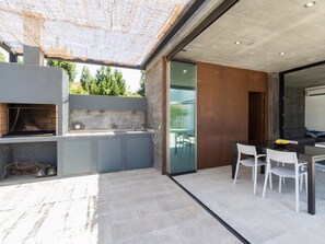 An outdoor kitchen area with a built-in grill, a dining table with chairs, and a glass door leading to a patio. - Exclusive Villa with garden and pool (Melegís)