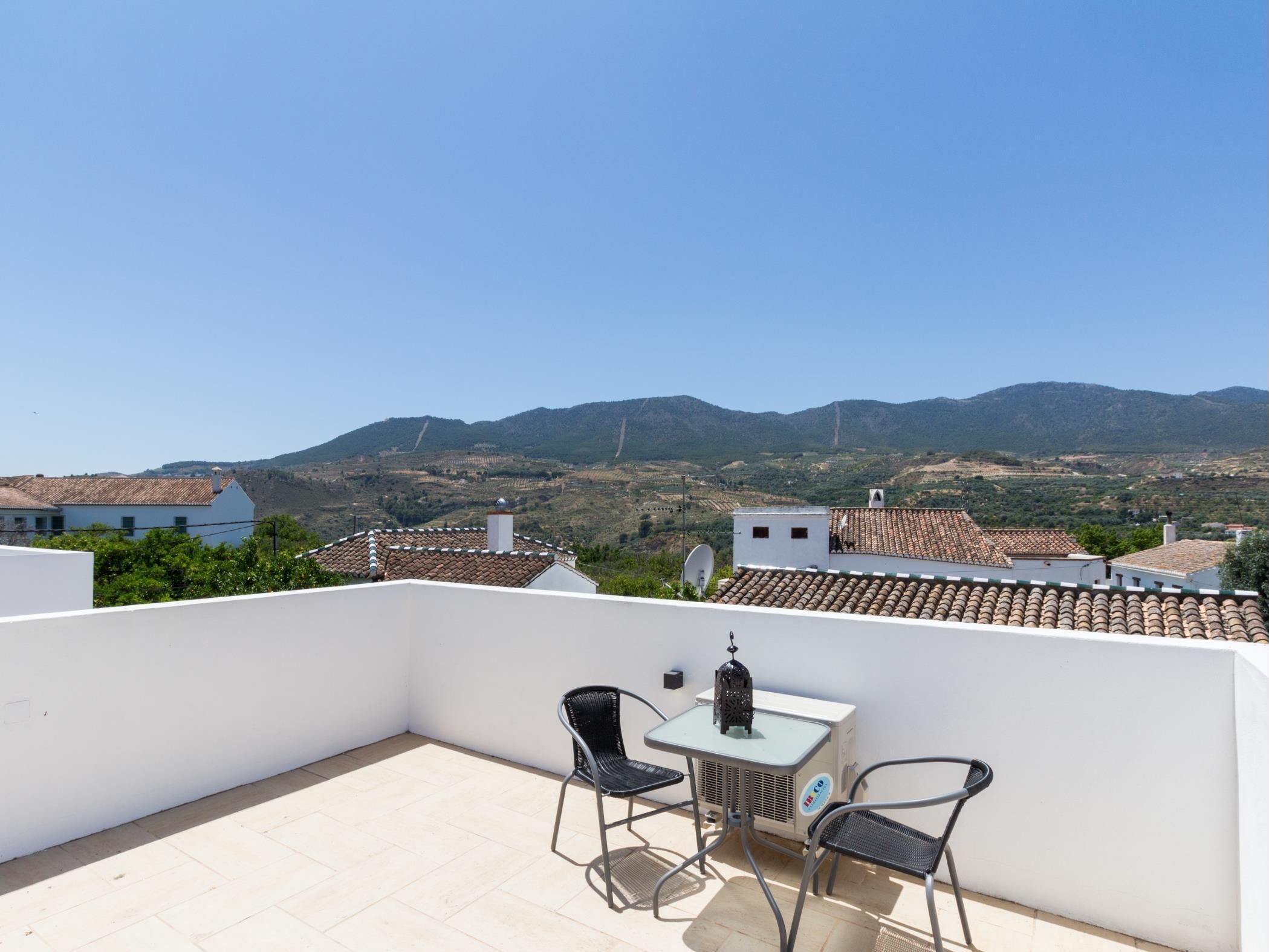 A rooftop terrace with a table and chairs, a satellite dish, and a view of distant mountains.