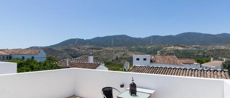 A rooftop terrace with a table and chairs, a satellite dish, and a view of distant mountains.