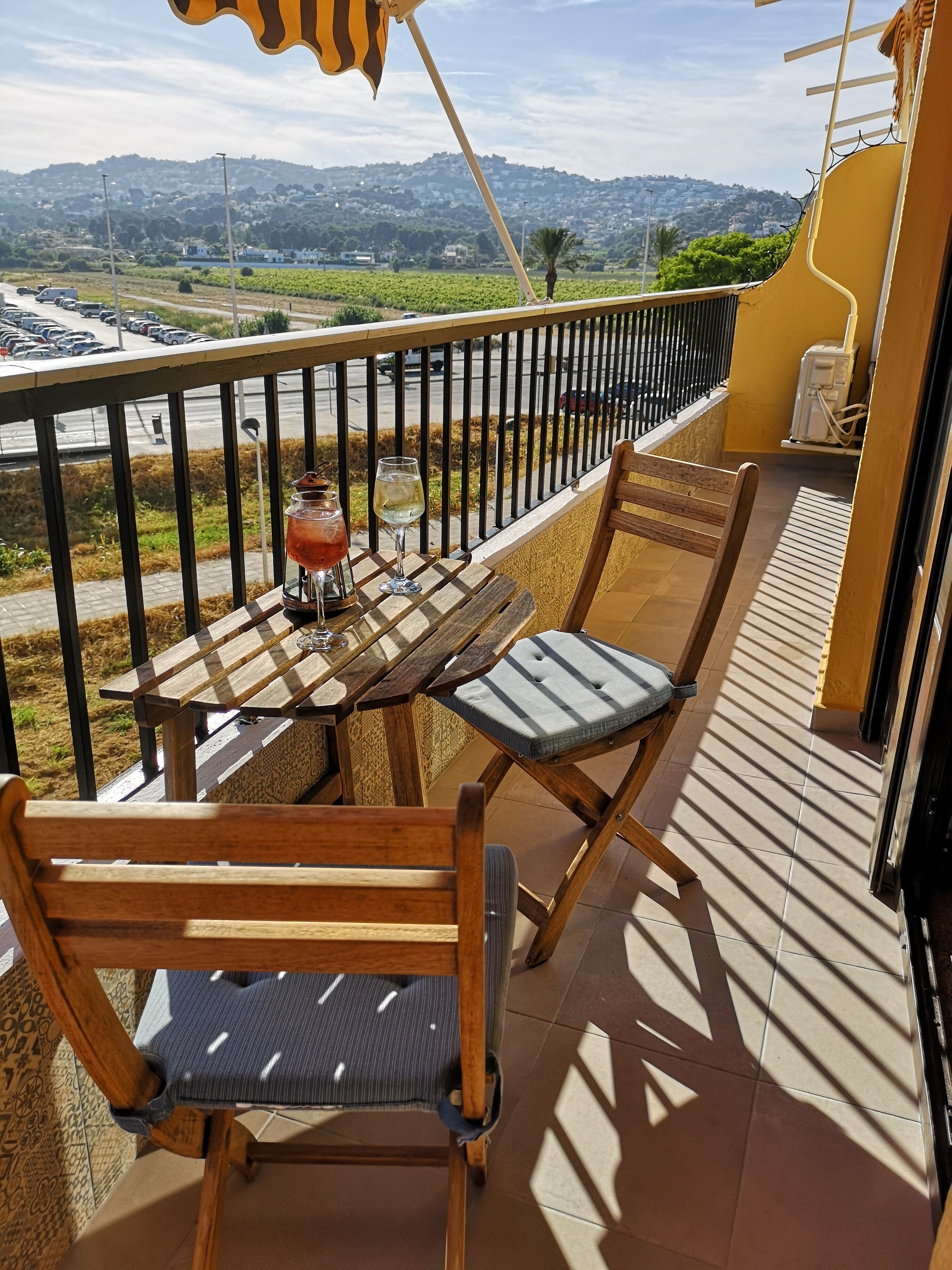 Un balcón con una mesa de madera y dos sillas, una copa de vino blanco y una copa de vino tinto.