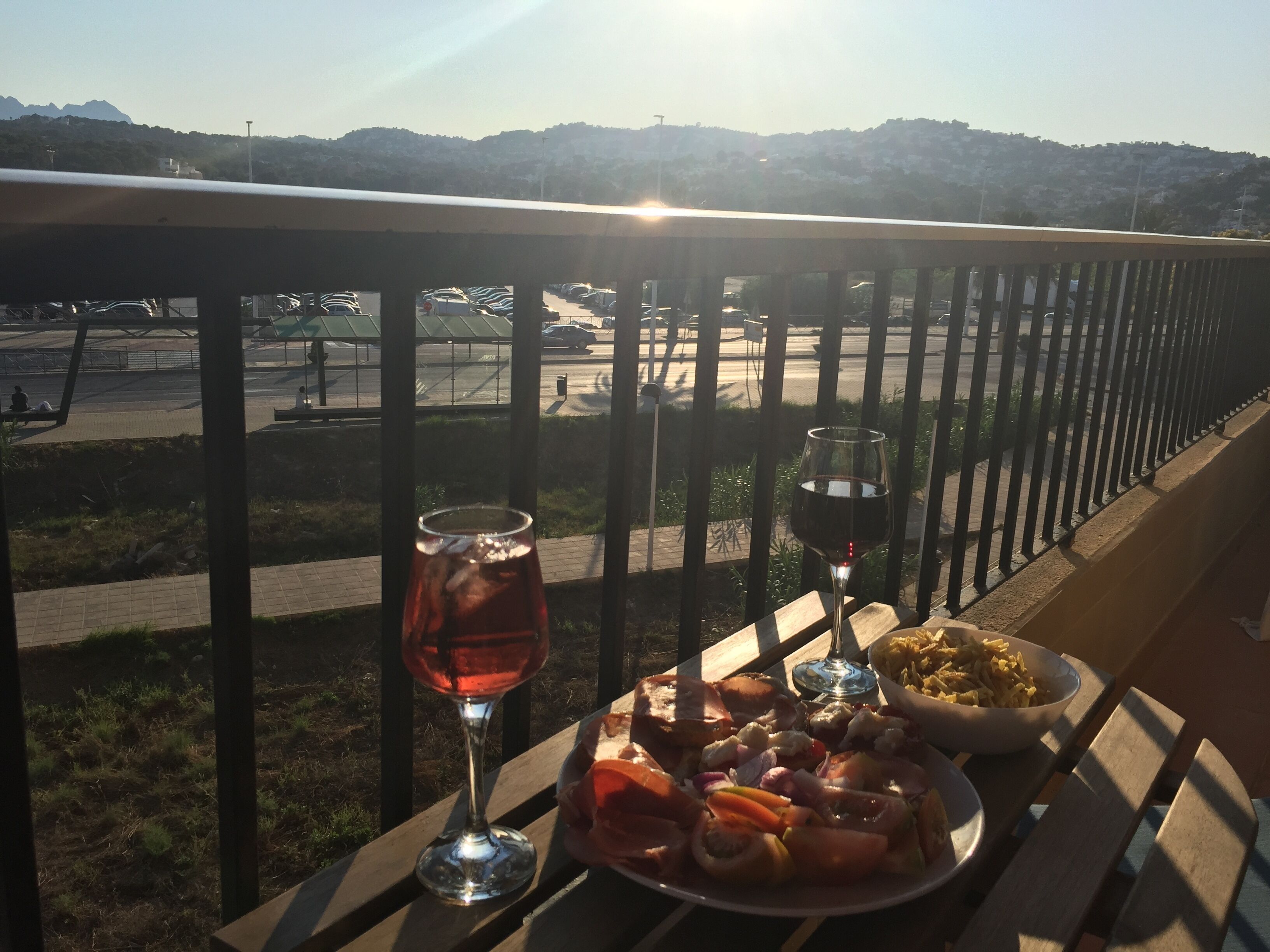Ein Balkon mit Tisch, gedeckt für eine Mahlzeit, einem Glas Rotwein und einer Schüssel Pasta.