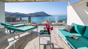 Eine Terrasse mit Meerblick, ein grünes Sofa, ein Tisch mit einer Serviertablett und zwei grüne Loungestühle.