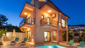 Ein zweistöckiges Haus mit Swimmingpool, Balkonen und Außenbereich zum Sitzen.
