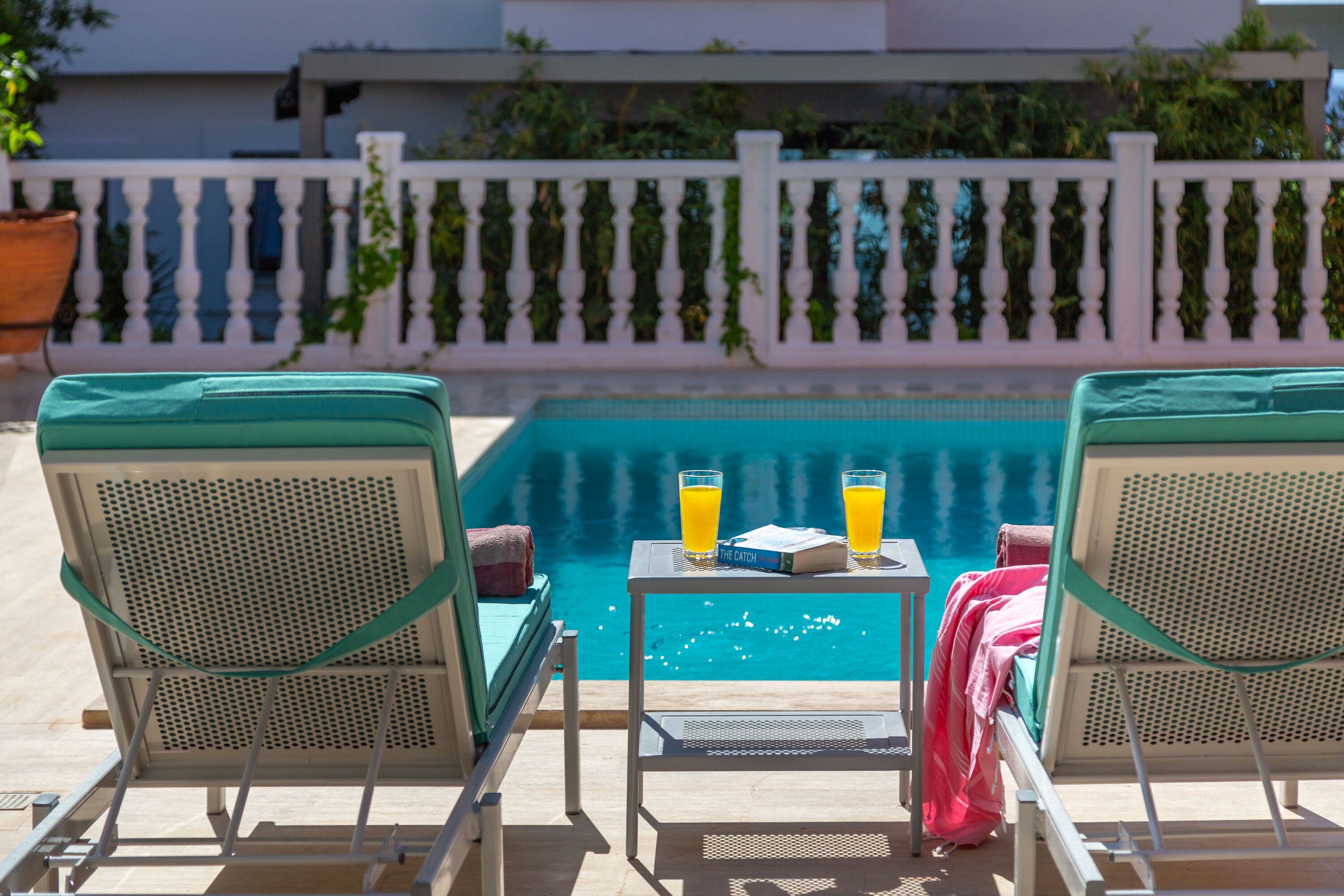 A poolside area with two lounge chairs, a table with drinks, and a book.