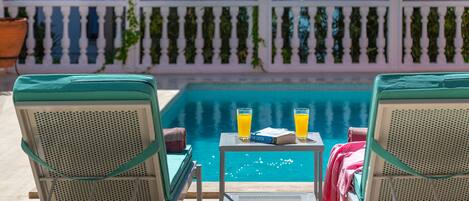 A poolside area with two lounge chairs, a table with drinks, and a book.