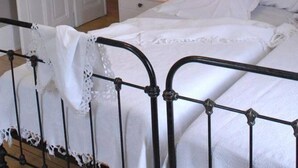 A bedroom with a metal bed frame, white bedding, a nightstand with a lamp, and a door leading to another room. - Beautiful mansion for 10 people (Le Val-D'ajol)