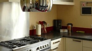 A kitchen with a gas stove, oven, and red chairs. There are three hanging light fixtures and a clock on the wall. - Beautiful mansion for 10 people (Le Val-D'ajol)