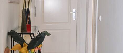 A hallway with a white door, a glass table with a vase of flowers, and a mirror on the wall.