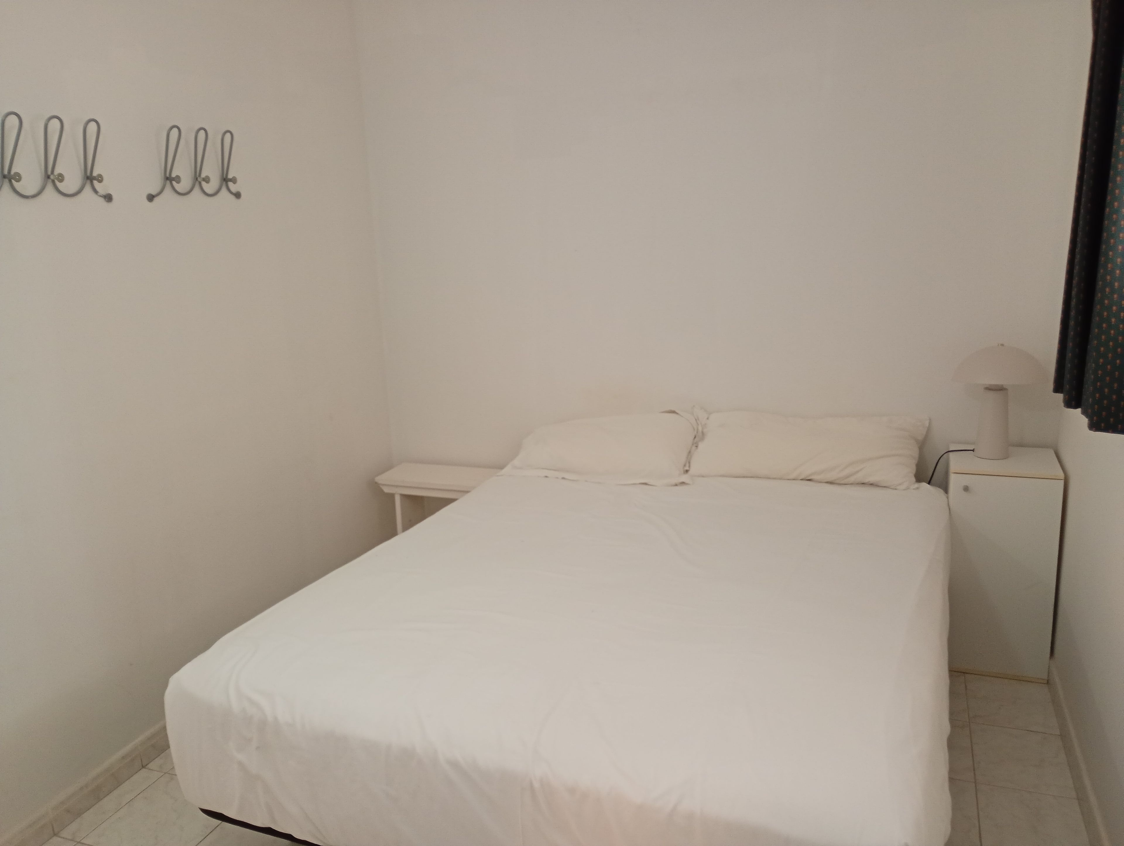 Een eenvoudige, schone kamer met een bed, nachtkastje en een wandlamp.