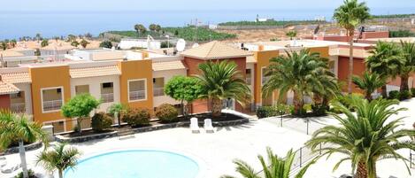 A residential area with a swimming pool surrounded by palm trees and a view of the sea.