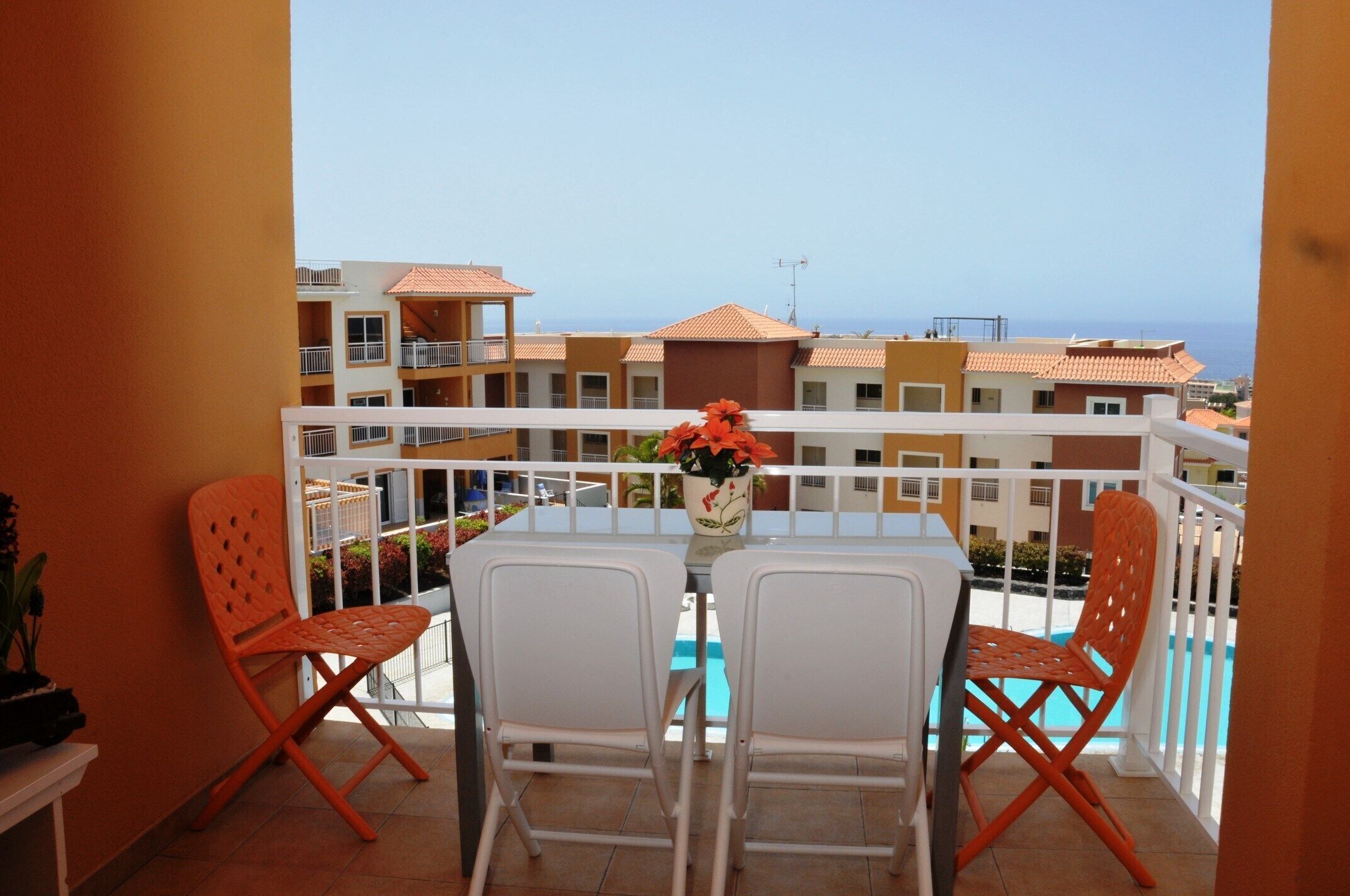 Un balcon avec une table et deux chaises, donnant sur une piscine et des immeubles.