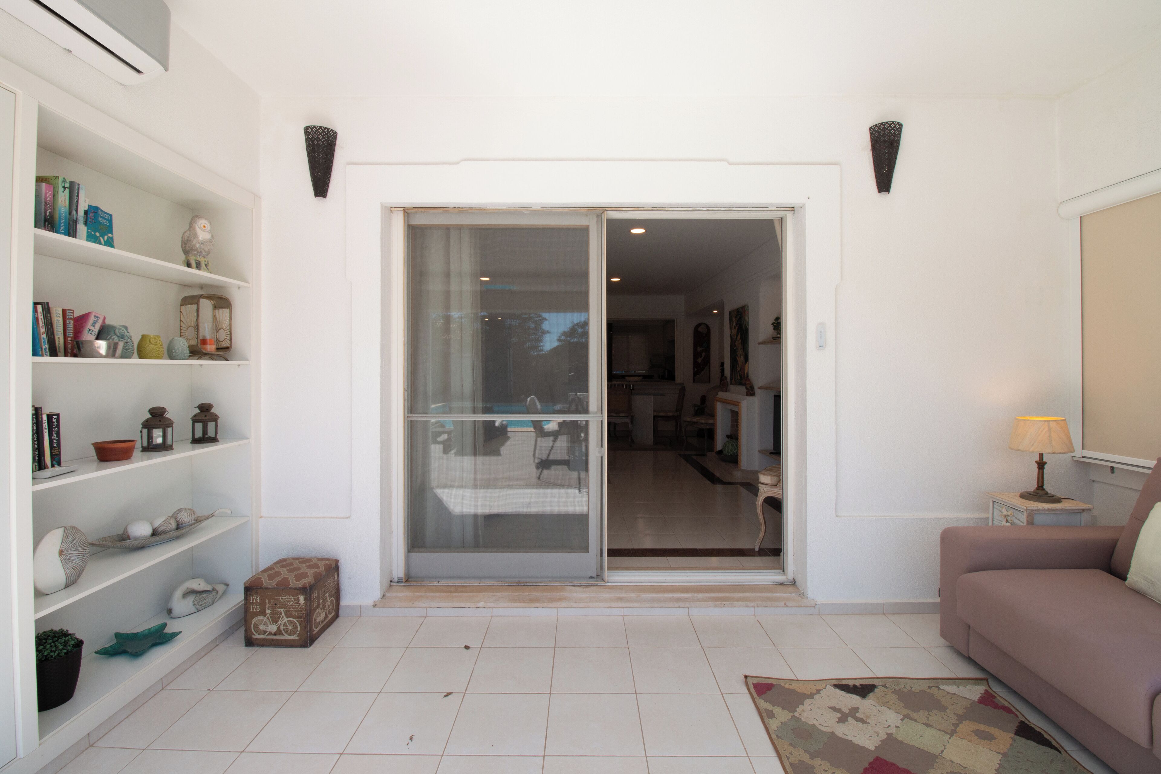 A living room with a sliding glass door leading to a dining area, a sofa, a lamp, and a bookshelf with various items.