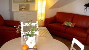 A cozy living room with a red sofa, a white coffee table with fruits, and a bookshelf. - Country Cottage / Gite - SCHERWILLER (Scherwiller)